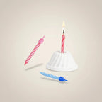 MUMSAN CANDLE 5 cm pembe ve mavi burgulu pasta mumları, biri yanan, altlık üzerinde ve havada.